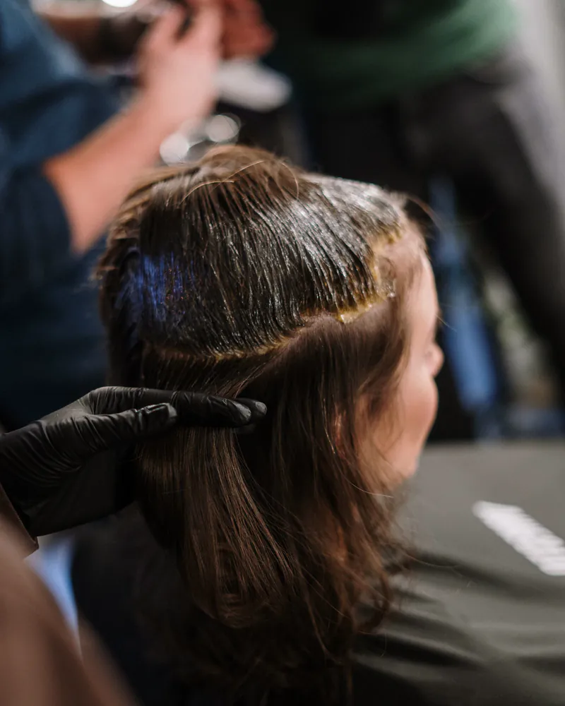 A stylist applying color from a bowl to a seated client's hair