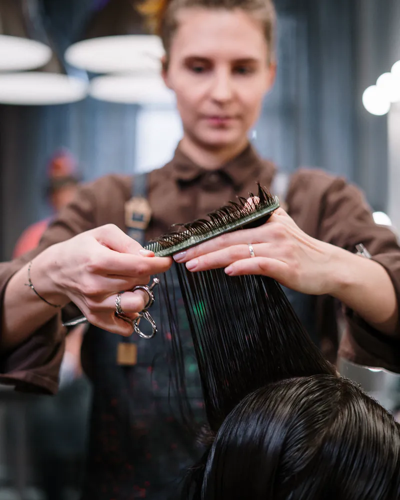 A stylist combing and cutting a seated client's hair