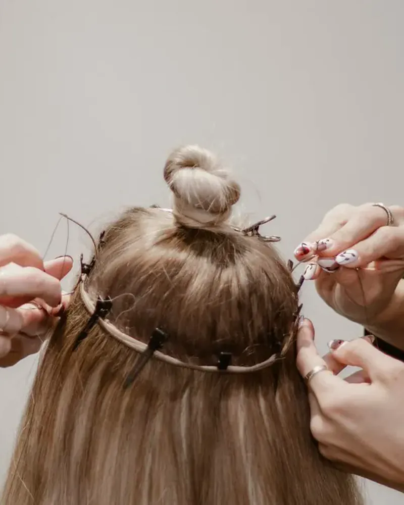 Two stylists hand tying wefts into a client's hair