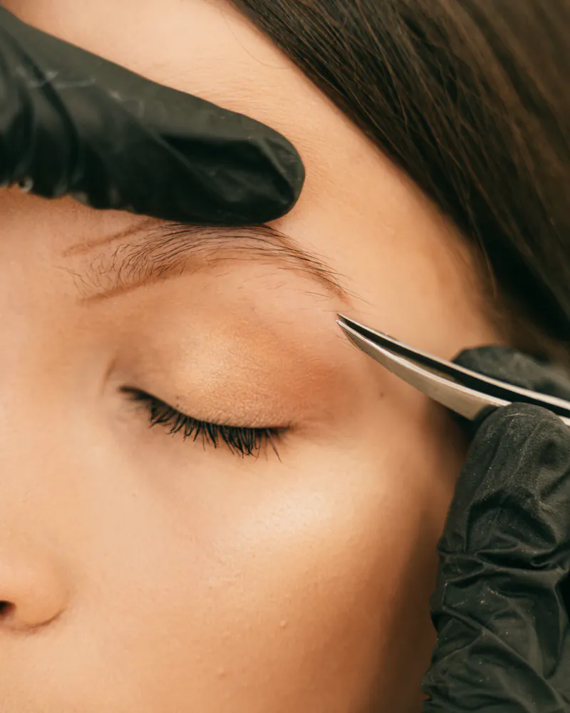 A technician shaping a client's eyebrow with tweezers