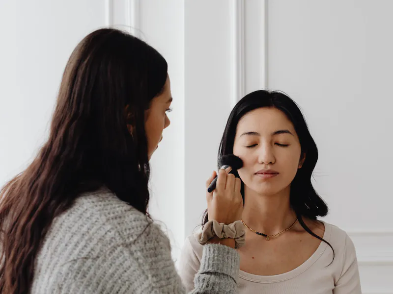 A makeup artist applying foundation to a seated client's face