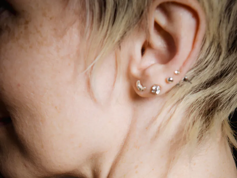 A studio close-up of an ear with several delicate stud and hoop piercings
