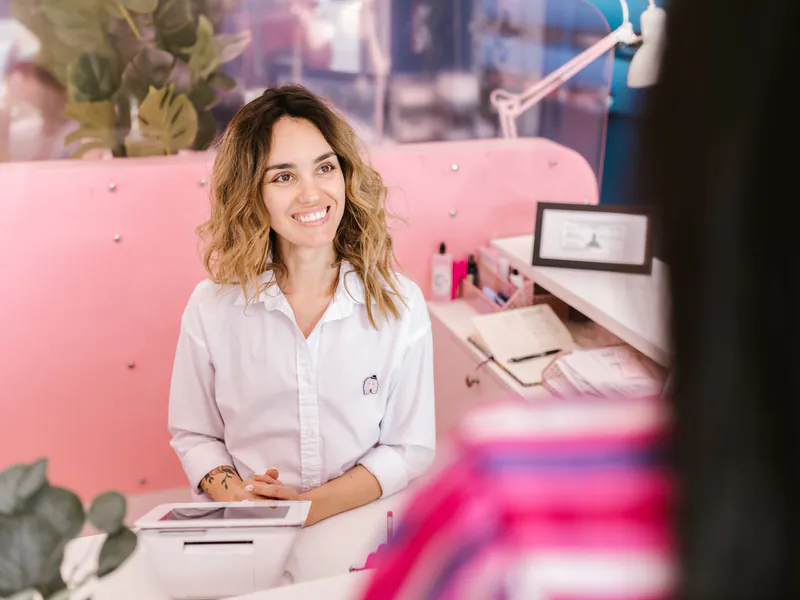 A smiling receptionist welcoming a client at a salon front desk