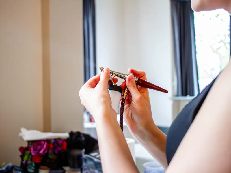 A professional holding a handheld airbrush tool near a client's face
